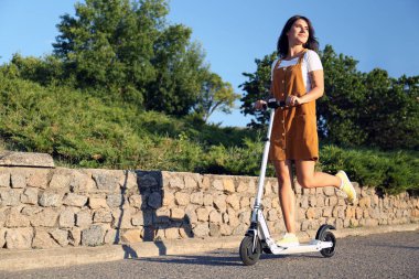 Genç bir kadın şehir caddesinde scooter sürüyor.
