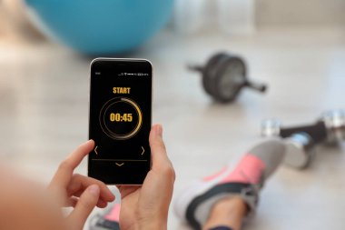 Genç bir kadın akıllı telefonunda spor uygulaması kullanıyor, kapalı mekanda, yakın plan. Metin için boşluk