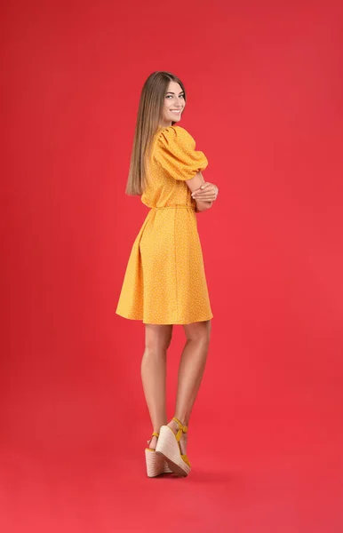 若いです女性身に着けているスタイリッシュな黄色のドレス上の赤の背景 — ストック写真