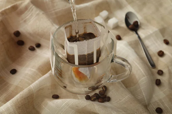 Heißes Wasser Glasbecher Mit Tropfkaffeesack Auf Beigem Stoff Gießen Nahaufnahme — Stockfoto