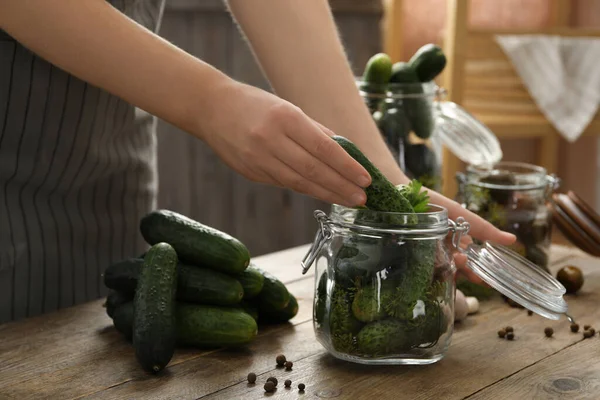 Woman putting cucumber into glass jar at wooden kitchen table, closeup. Pickling vegetables — Stock Image Woman Putting Cucumber Glass Jar Wooden Kitchen Table Closeup Pickling Royalty Free Stock Images