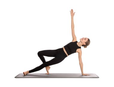 Spor kıyafetli genç bir kadın beyaz arka planda yoga yapıyor.