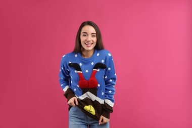 Pembe arka planda Noel süveteri giyen genç bir kadın.