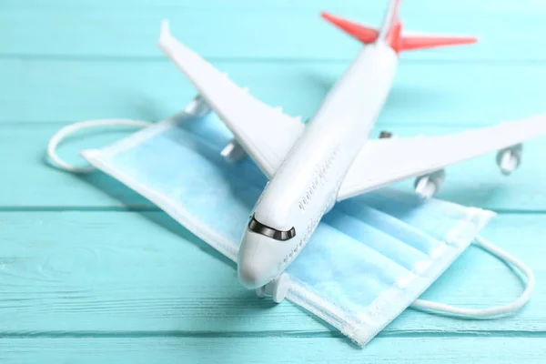 Toy airplane and medical mask on light blue wooden background, closeup. Travelling during coronavirus pandemic