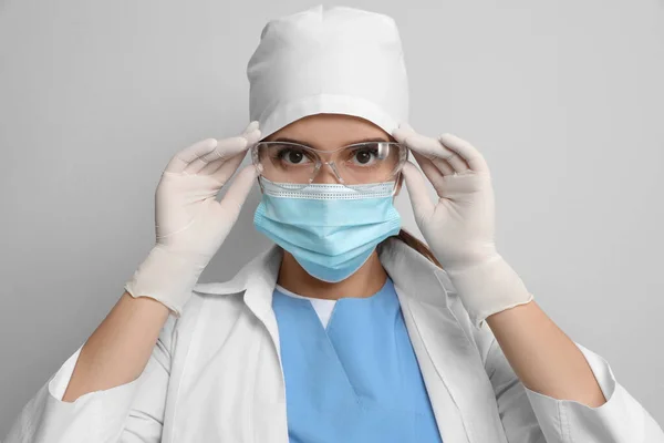 Dokter Beschermend Masker Medische Handschoenen Zetten Bril Tegen Lichtgrijze Achtergrond — Stockfoto