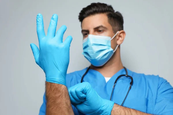 Arzt Schutzmaske Zieht Medizinische Handschuhe Vor Hellgrauem Hintergrund — Stockfoto