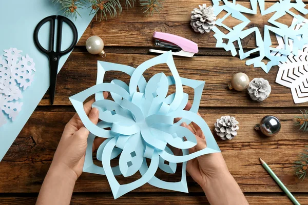 Woman making paper snowflake at wooden table, top view
