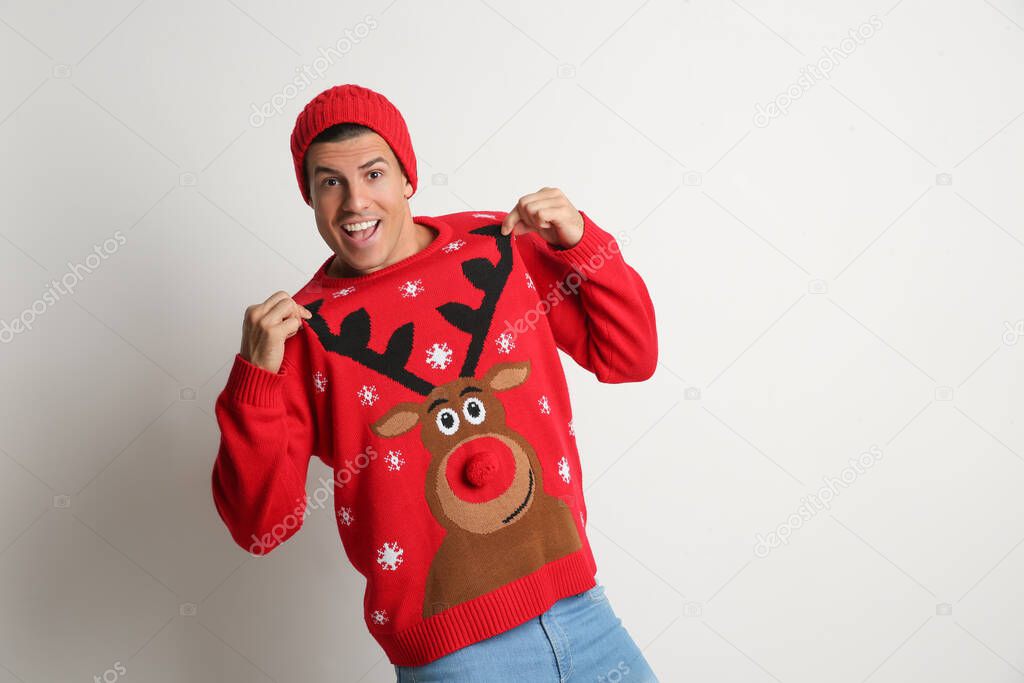 Happy man in hat showing his Christmas sweater on white background, space for text