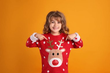 Kırmızı Noel süveterini turuncu arka planda gösteren sevimli küçük kız.