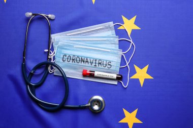 Stetoskop, koruyucu maskeler ve Avrupa Birliği bayraklarında kan örneği olan test tüpü, düz konum. Coronavirüs salgını