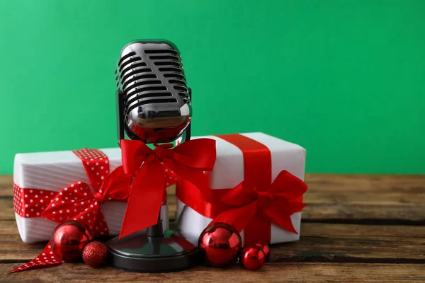 Retro microphone with red bow, gift boxes and festive decor on wooden table against green background, space for text. Christmas music