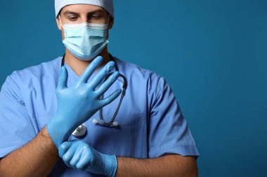 Koruyucu maskeli doktor mavi arka planda tıbbi eldiven takıyor.