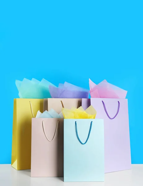 Kleurrijke Geschenkzakjes Met Papier Witte Tafel Tegen Lichtblauwe Achtergrond — Stockfoto