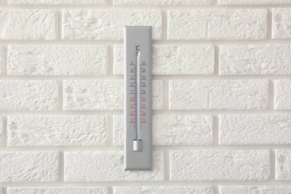 Weather thermometer hanging on white brick wall