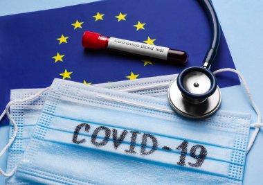 Avrupa Birliği bayrağı, koruyucu maskeler, steteskop ve açık mavi arka planda kan örneği olan test tüpü. Coronavirüs salgını