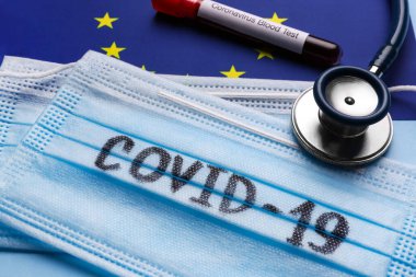 Koruyucu maskeler, steteskop ve Avrupa Birliği bayraklarında kan örneği olan test tüpü, yakın plan. Coronavirüs salgını