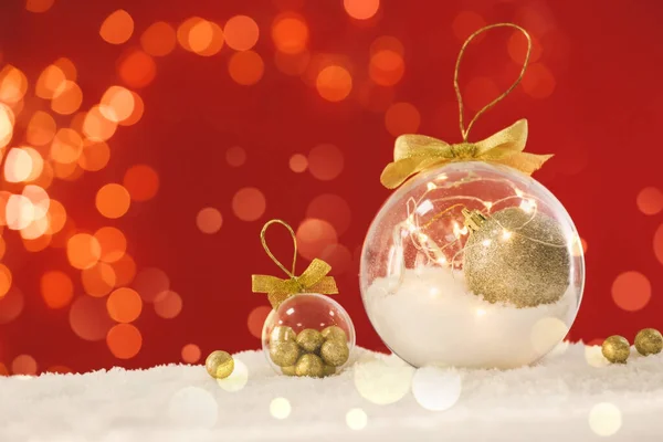 Schöne Transparente Weihnachtsschmuck Mit Goldenen Schleifen Auf Schnee Vor Rotem — Stockfoto