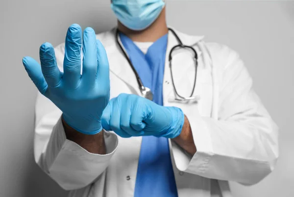 Dokter Beschermende Masker Zetten Medische Handschoenen Tegen Lichtgrijze Achtergrond Close — Stockfoto