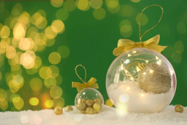 Όμορφη Διαφανή Χριστουγεννιάτικα Στολίδια Χρυσά Τόξα Στο Χιόνι Πράσινο Φόντο — Φωτογραφία Αρχείου