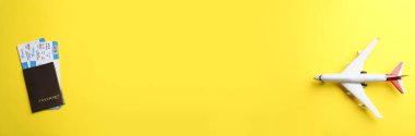 Sarı arka planda biletleri olan oyuncak uçak ve pasaport.