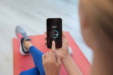 Genç bir kadın akıllı telefonunda spor uygulaması kullanıyor. Kapalı alanda.