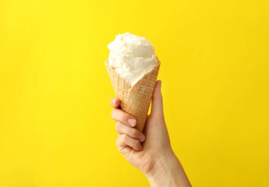 Sarı arka planda lezzetli dondurmalı waffle külahı tutan kadın, yakın plan.