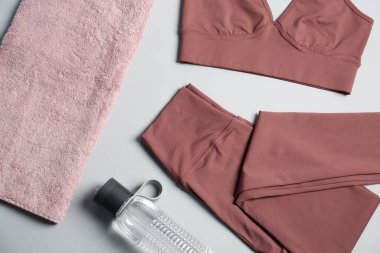 Spor kıyafetleri, gri arka planda bir şişe su ve havlu, düz yatış. Yoga ekipmanları
