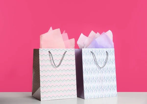 Gift bags with paper on white table against pink background