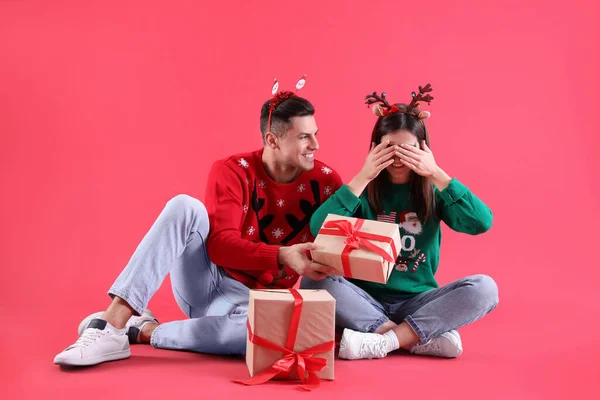 美しい幸せなカップルでクリスマスのヘッドバンドとセーター座ってギフトで赤の背景 — ストック写真