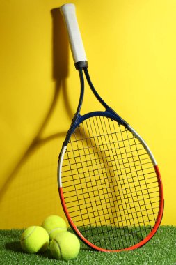 Tenis raketi ve toplar yeşil çimlere karşı sarı arka plan. Spor malzemeleri.