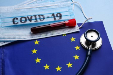 Avrupa Birliği bayrağı, koruyucu maskeler ve açık mavi arka planda kan örneği olan test tüpü. Coronavirüs salgını