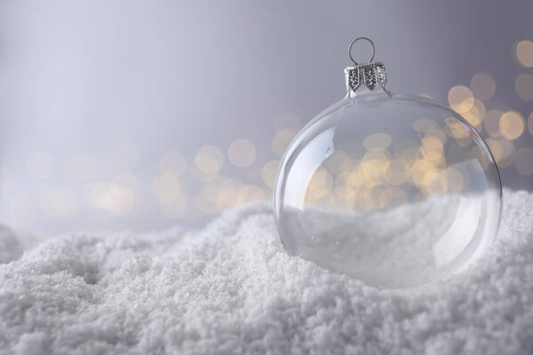 Transparent Christmas ball on snow against blurred fairy lights, space for text