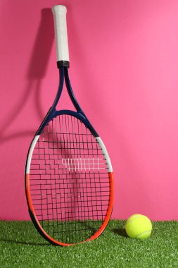 Tenis raketi ve top yeşil çimlerin üzerinde pembe arka plana karşı. Spor malzemeleri.