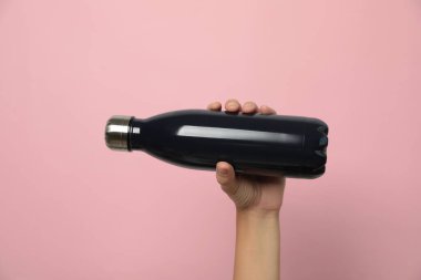 Pembe arka planda modern siyah termos tutan kadın, yakın plan.