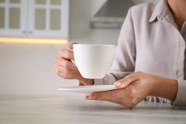 Beyaz bardaklı ve çay tabaklı kadın, kapalı bir masada, yakın plan.