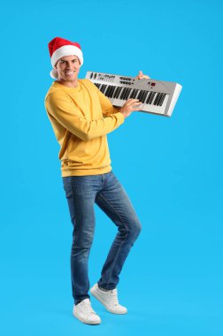 Noel Baba şapkalı bir adam açık mavi arka planda sentezleyici çalıyor. Noel müziği