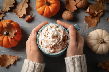 Gri ahşap masada nefis balkabaklı latte tutan bir kadın.