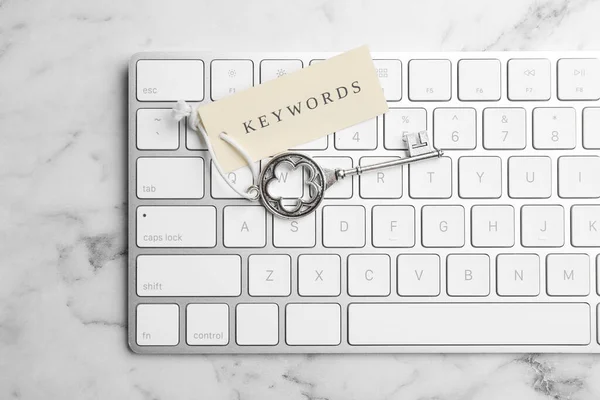 Keyboard, vintage key and tag with word KEYWORDS on white marble table, top view