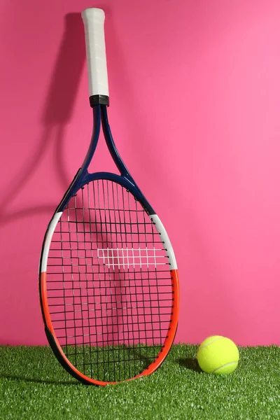 Tenis raketi ve top yeşil çimlerin üzerinde pembe arka plana karşı. Spor malzemeleri.