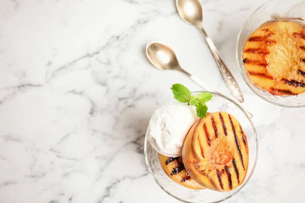 Delicious grilled peaches with ice cream and mint on white marble table, flat lay. Space for text