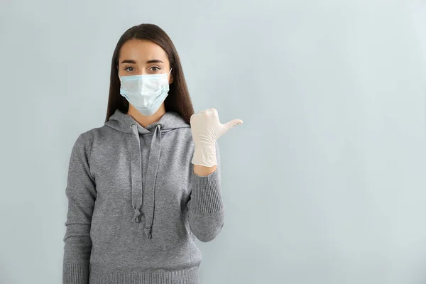 Kvinna Skyddande Ansiktsmask Och Medicinska Handskar Pekar Något Grå Bakgrund — Stockfoto