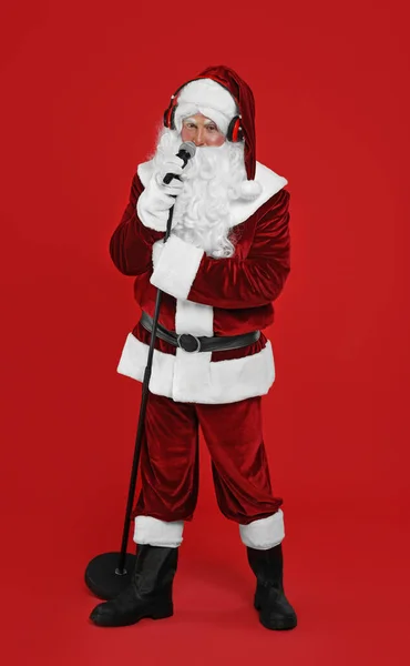 Święty Mikołaj Słuchawkami Mikrofonem Czerwonym Tle Muzyka Świąteczna — Zdjęcie stockowe
