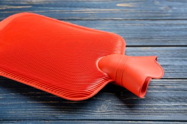 Mavi ahşap arka planda kırmızı lastik su şişesi, yakın plan.