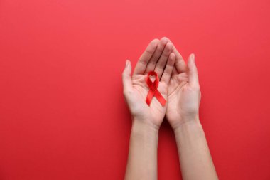 Renk arkaplanında kırmızı farkındalık kurdelesi tutan bir kadın. Üst görünümde yazı için boşluk var. Dünya AIDS Hastalıkları Günü