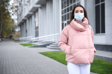 Sağlık maskeli genç bir kadın dışarıda yürüyor. COVID-19 salgını sırasında kişisel koruma