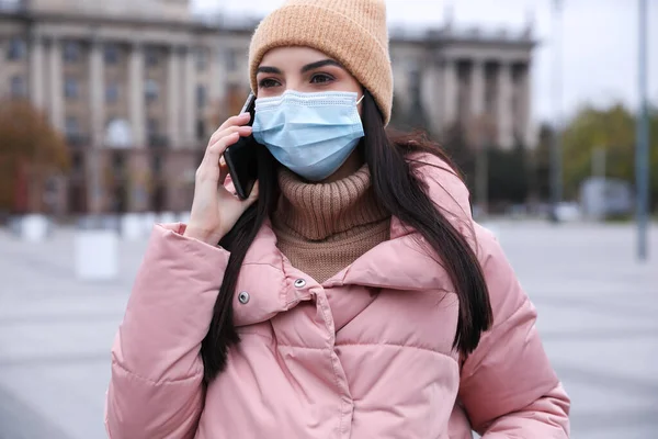 屋外を歩いている間に電話で話す医療面マスクの若い女性 Covid 19パンデミック時の個人情報保護 — ストック写真