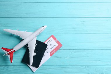 Toy airplane and passport with ticket on light blue wooden background, flat lay. Space for text