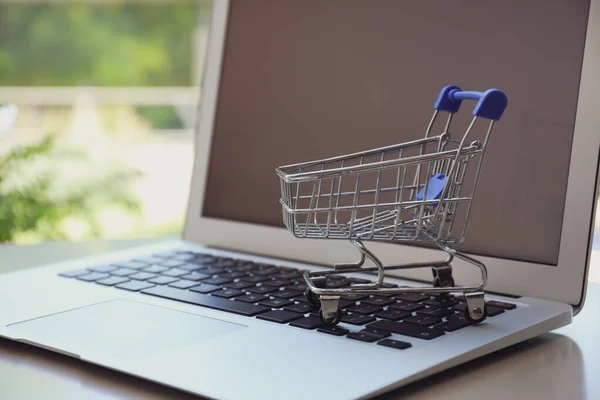 Internet shopping. Laptop with small cart on table indoors, closeup