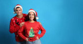 Pár v vánoční svetry a Santa klobouky na modrém pozadí, prostor pro text