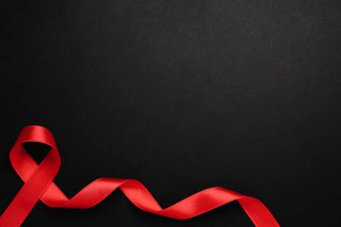 Siyah arkaplanda kırmızı kurdelenin üst görünümü, metin için boşluk. AIDS Hastalığı Farkındalığı